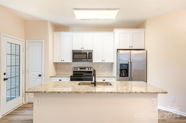 kitchen featuring light stone counters, a center island with sink, white cabinets, and stainless steel appliances