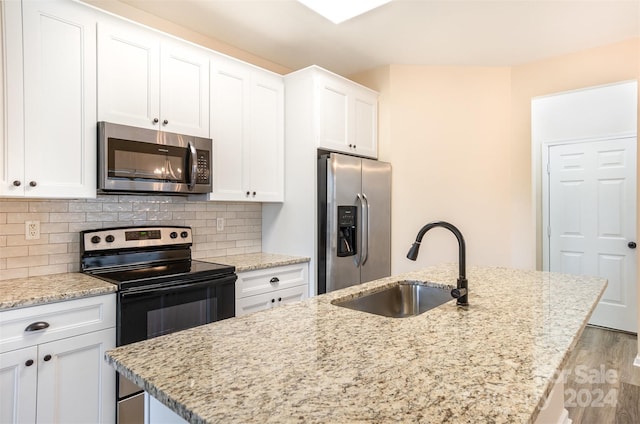 kitchen featuring light wood-type flooring, stainless steel appliances, white cabinetry, and a center island with sink