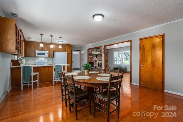 dining area featuring a fireplace, light hardwood / wood-style floors, a textured ceiling, and ornamental molding