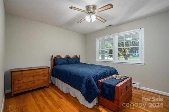 bedroom featuring ceiling fan, light hardwood / wood-style flooring, a textured ceiling, and a baseboard heating unit