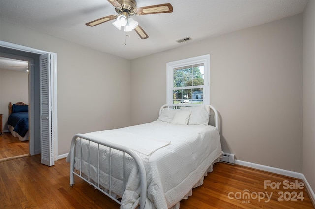 bedroom with ceiling fan, dark wood-type flooring, and a baseboard heating unit