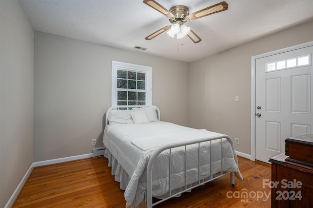 bedroom featuring hardwood / wood-style flooring, ceiling fan, and a baseboard heating unit