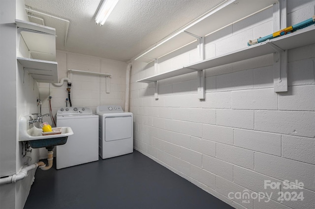 laundry area with a textured ceiling, washer and clothes dryer, and sink