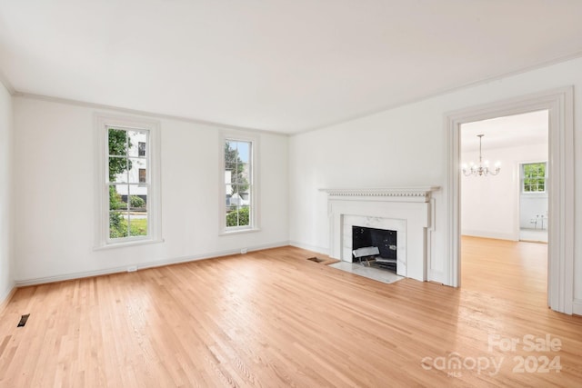 unfurnished living room featuring a wealth of natural light, an inviting chandelier, a premium fireplace, and hardwood / wood-style flooring