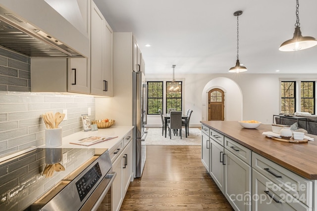 kitchen with a healthy amount of sunlight, dark hardwood / wood-style flooring, wall chimney range hood, and hanging light fixtures