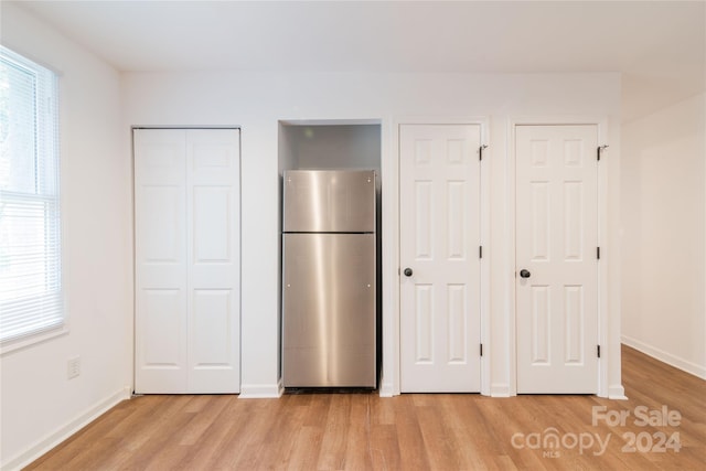 unfurnished bedroom featuring light wood-type flooring, stainless steel refrigerator, and two closets