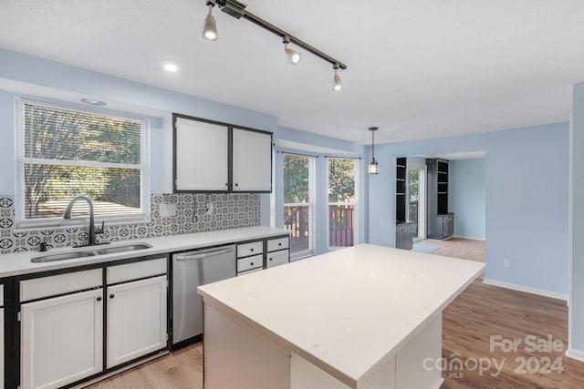 kitchen featuring light wood-type flooring, stainless steel dishwasher, sink, decorative light fixtures, and a center island