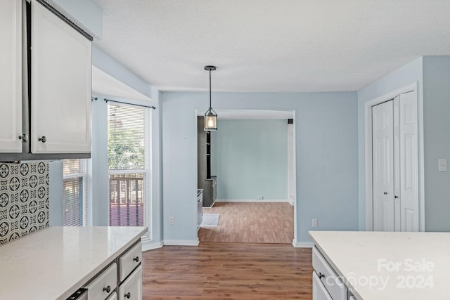 kitchen with pendant lighting, white cabinets, hardwood / wood-style flooring, light stone countertops, and a textured ceiling