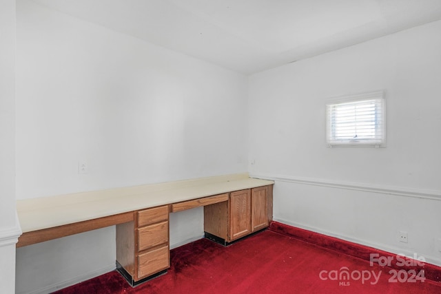 unfurnished office featuring dark colored carpet and built in desk