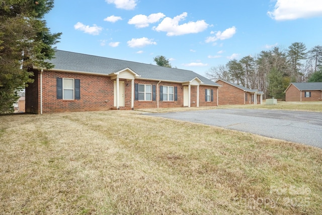 ranch-style house featuring roof with shingles, brick siding, a front lawn, and aphalt driveway