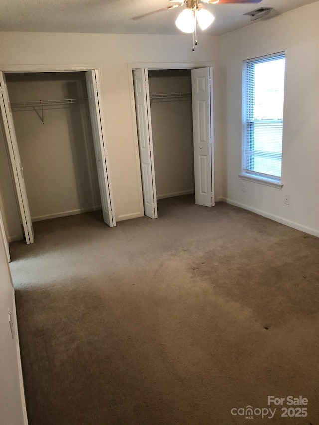 unfurnished bedroom featuring baseboards, visible vents, a ceiling fan, light colored carpet, and two closets