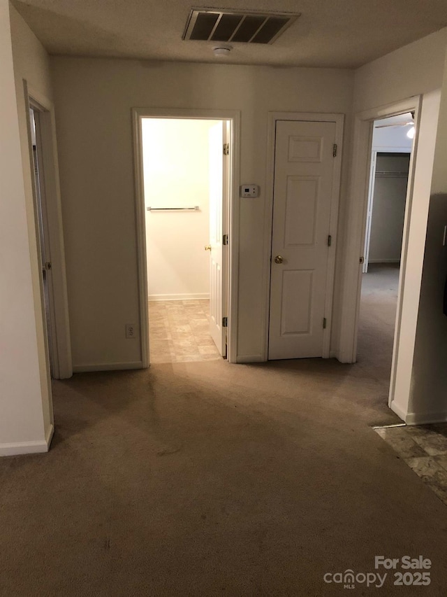 corridor with light carpet, visible vents, and baseboards