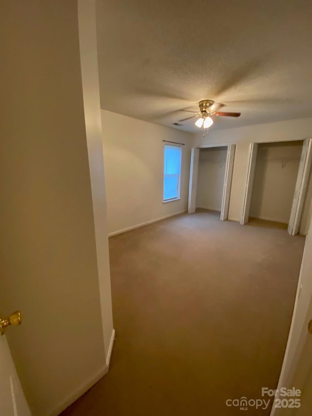 unfurnished bedroom with a textured ceiling, light carpet, baseboards, and multiple closets