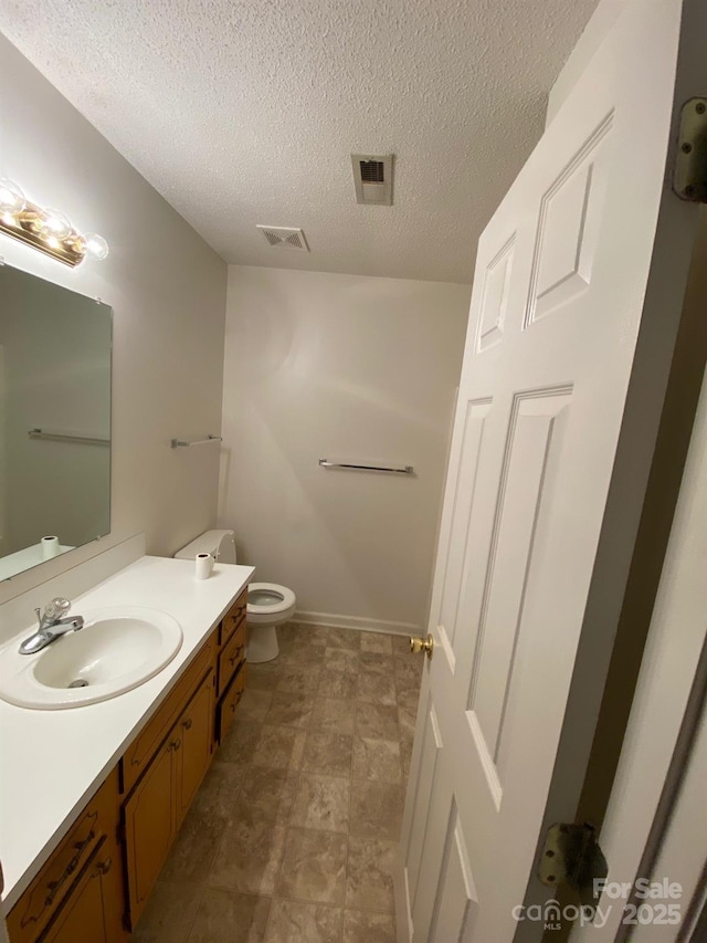 half bath featuring toilet, visible vents, a textured ceiling, and vanity