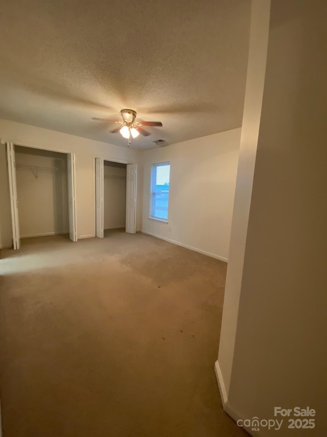 unfurnished bedroom with carpet, two closets, a ceiling fan, a textured ceiling, and baseboards