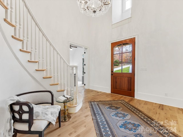 entrance foyer featuring ceiling fan with notable chandelier, a towering ceiling, and light hardwood / wood-style flooring