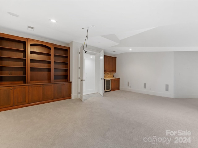 unfurnished living room with vaulted ceiling, light colored carpet, and wine cooler