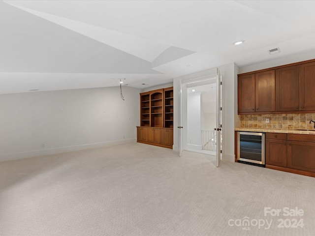 interior space with lofted ceiling, light carpet, sink, tasteful backsplash, and beverage cooler