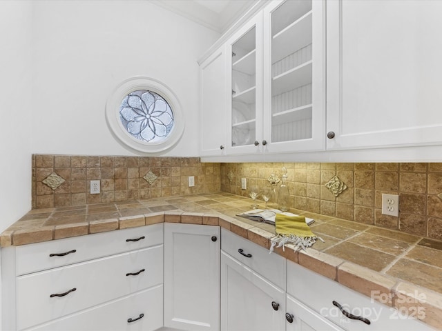 kitchen with white cabinetry, ornamental molding, tile counters, and decorative backsplash