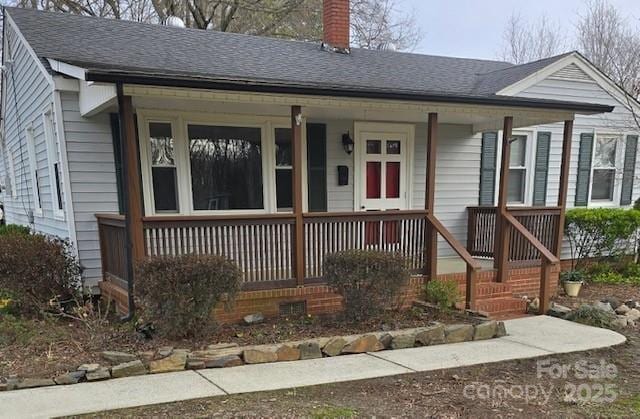 view of front of house with covered porch, roof with shingles, and a chimney