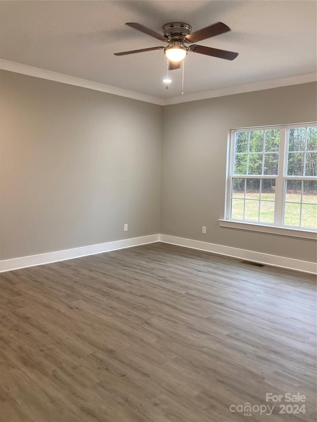 empty room with crown molding, ceiling fan, and dark wood-type flooring