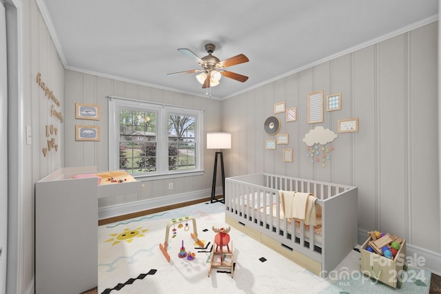 bedroom featuring ceiling fan, wood-type flooring, crown molding, and a nursery area