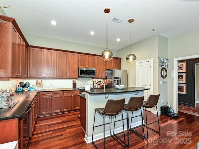 kitchen with appliances with stainless steel finishes, backsplash, dark hardwood / wood-style flooring, a kitchen island with sink, and pendant lighting