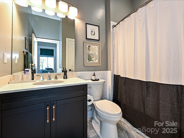 bathroom featuring walk in shower, vanity, toilet, and tile walls