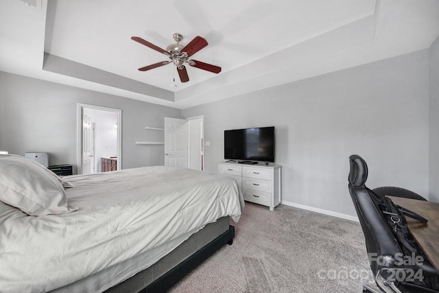 bedroom featuring ceiling fan, light carpet, connected bathroom, and a tray ceiling