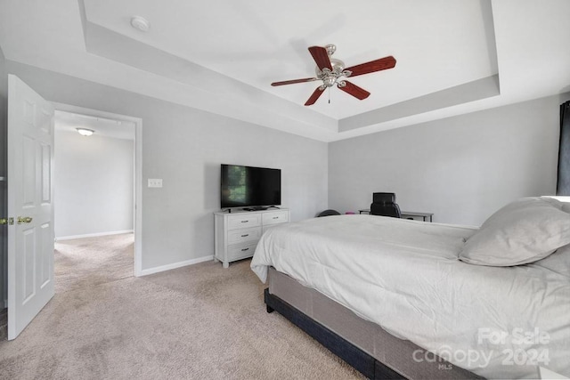 carpeted bedroom with a raised ceiling and ceiling fan