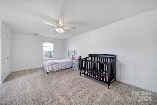 bedroom with light carpet, a nursery area, and ceiling fan