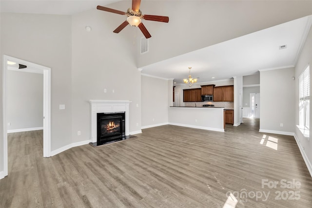 unfurnished living room with visible vents, baseboards, light wood-style floors, a glass covered fireplace, and crown molding