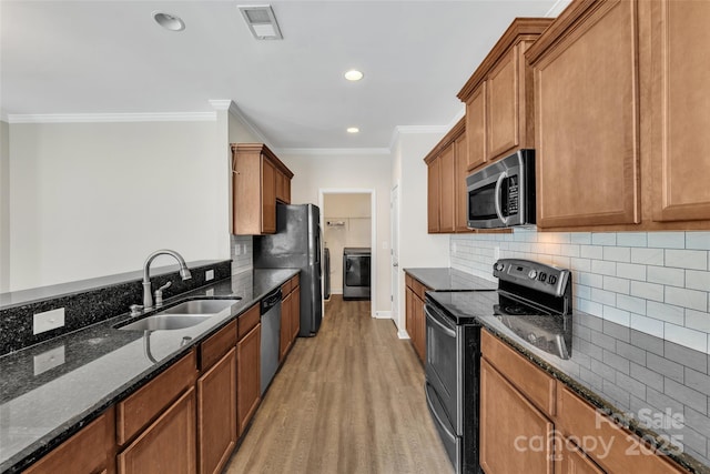 kitchen with dark stone counters, appliances with stainless steel finishes, crown molding, light wood-style floors, and a sink