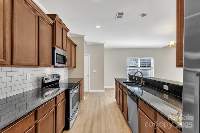 kitchen featuring visible vents, appliances with stainless steel finishes, brown cabinetry, a sink, and dark stone counters