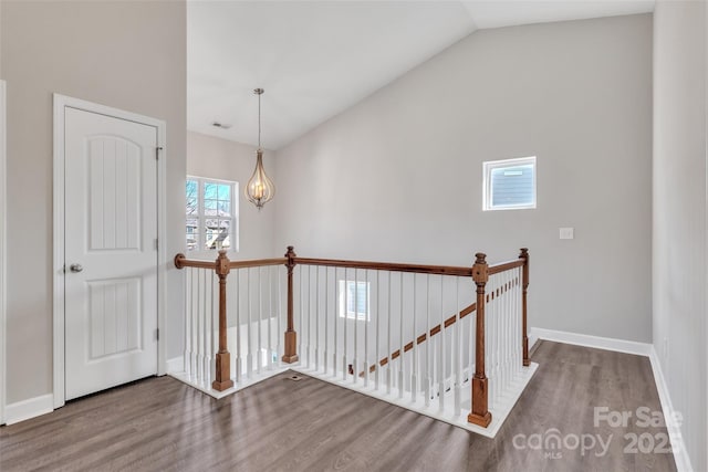 hall with visible vents, baseboards, lofted ceiling, wood finished floors, and an upstairs landing