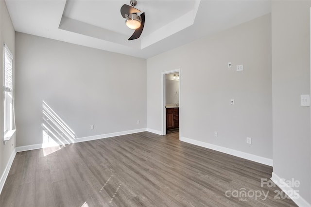 empty room with a tray ceiling, baseboards, and wood finished floors