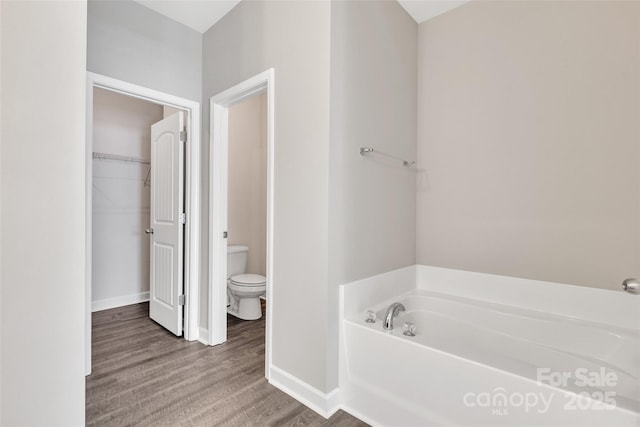 bathroom featuring a walk in closet, toilet, wood finished floors, baseboards, and a bath