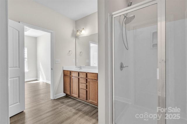 bathroom with a stall shower, wood finished floors, vanity, and baseboards