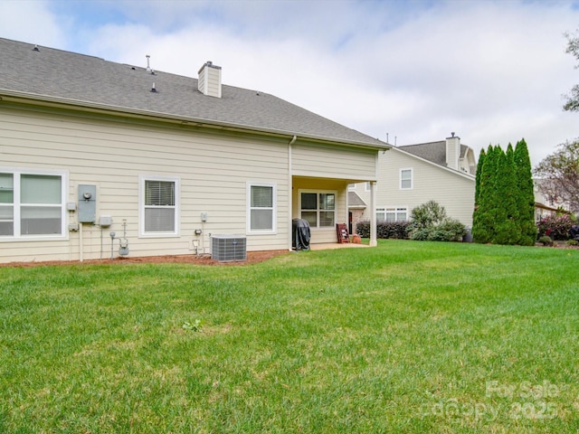 rear view of property with central AC, a yard, a chimney, and a shingled roof