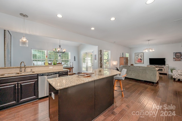 kitchen with light stone counters, decorative light fixtures, dark wood-type flooring, stainless steel dishwasher, and a kitchen island with sink