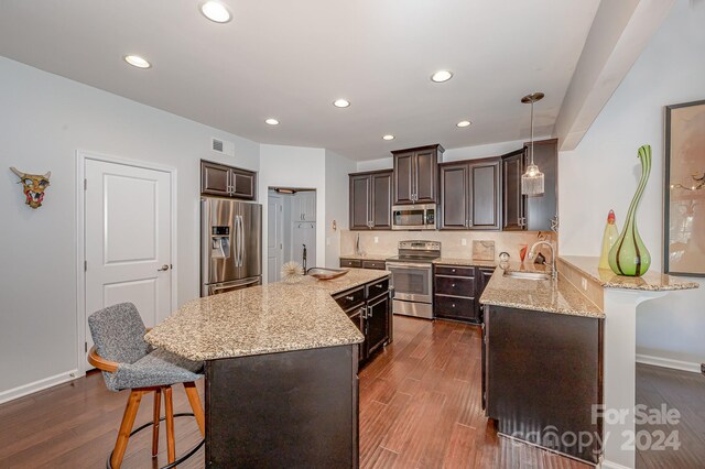 kitchen featuring appliances with stainless steel finishes, decorative light fixtures, dark hardwood / wood-style flooring, a breakfast bar area, and kitchen peninsula