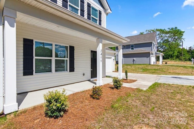 view of exterior entry featuring a porch, concrete driveway, a yard, and a garage