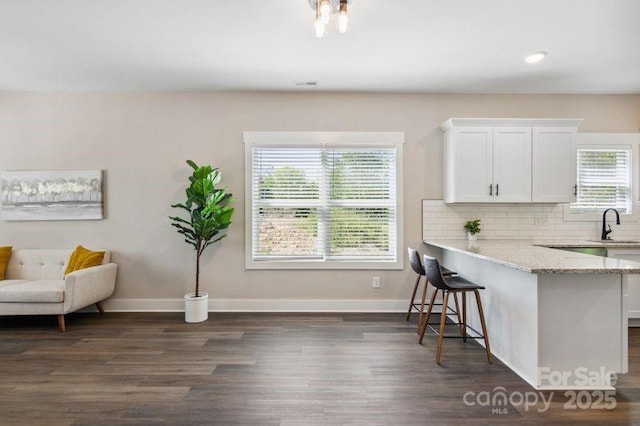 kitchen with light stone counters, baseboards, white cabinets, a kitchen breakfast bar, and backsplash