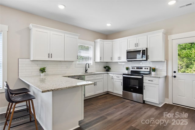 kitchen featuring visible vents, a sink, white cabinetry, stainless steel appliances, and a peninsula