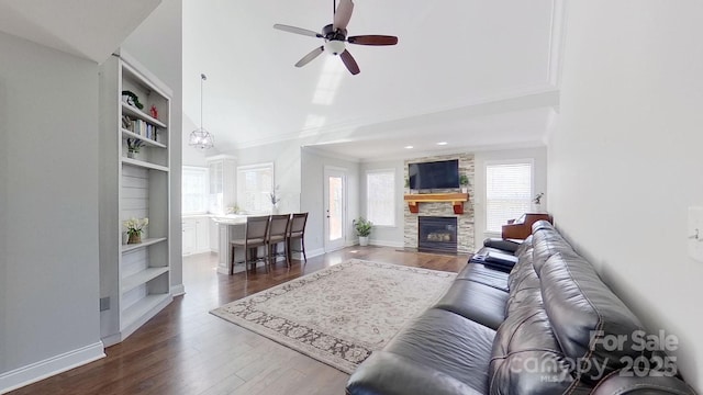 living room with ceiling fan, dark hardwood / wood-style floors, built in features, and a stone fireplace