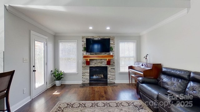 living room featuring dark hardwood / wood-style flooring, a healthy amount of sunlight, ornamental molding, and a stone fireplace