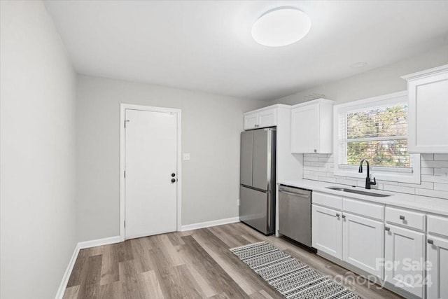 kitchen with backsplash, white cabinets, sink, light hardwood / wood-style flooring, and stainless steel appliances