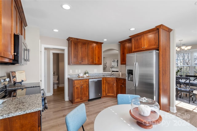 kitchen with light stone counters, stainless steel appliances, sink, a notable chandelier, and light hardwood / wood-style floors