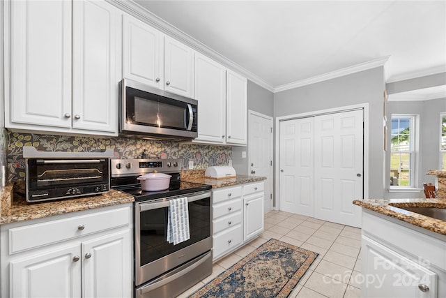 kitchen with light stone countertops, stainless steel appliances, white cabinets, crown molding, and light tile patterned flooring