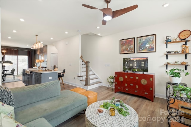 living room featuring ceiling fan with notable chandelier and light hardwood / wood-style floors